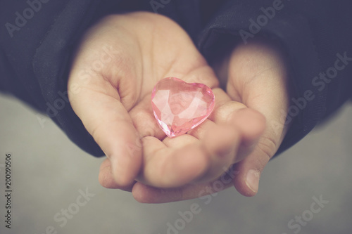 baby hands holding a glass pink heart