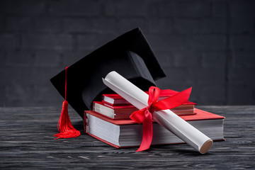 Stacked books with diploma and graduation hat on table