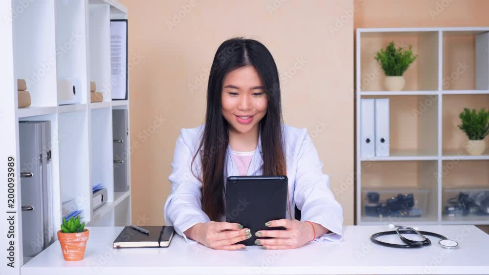 doctor holding digital tablet using app for online consultation. asian woman wearing white lab coat sitting in the office has video chat with patient or colleagues