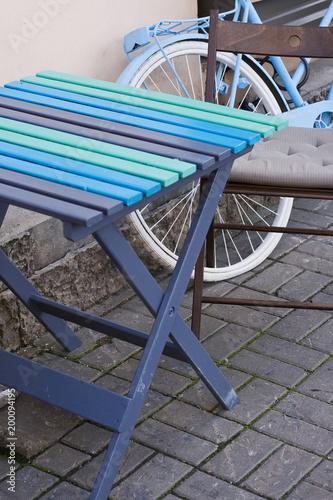 Outdoor cafe, street stone floor, table and chair, white wheel of blue bicycle. Pastel colours. Vintage style. Modern view. Selective focus.