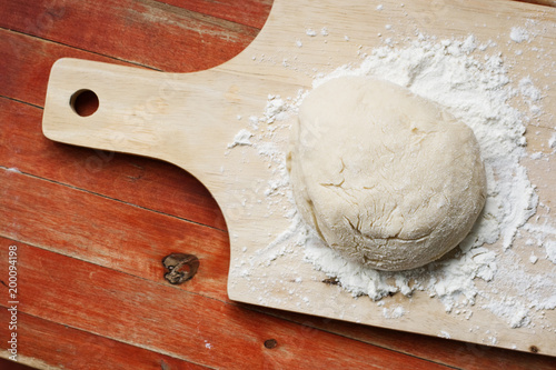 The process of cooking pizza, pies, tarts or buns. Ball of dough on the table. The wooden board covered with flour. Wooden background, painted red, old weathered natural wood.