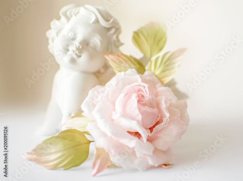 Beautiful flower in light pink cream and white colors rose hand made on white blurred background with angel or amur statuette. Vintage retro style card or decoration. Fashionable female corsage brooch