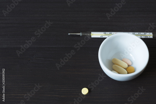 Medications and thermometer on wooden background