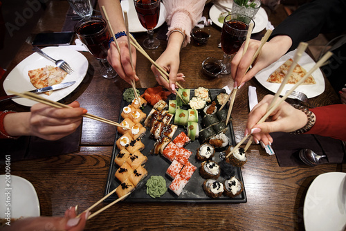A set of sushi rolls on a table in a restaurant. A party of friends eating sushi rolls using bamboo sticks.