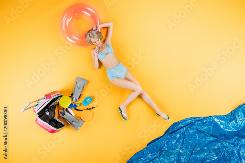 top view of beautiful girl in swimsuit and flip flops lying on inflatable ring on yellow