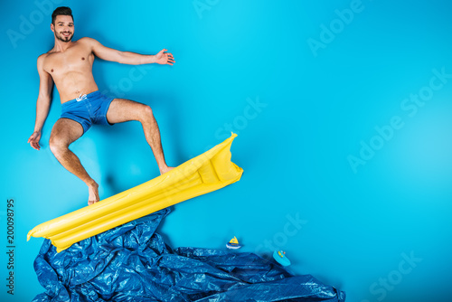 Konstfotografi handsome young man in shorts smiling at camera while standing on inflatable matt