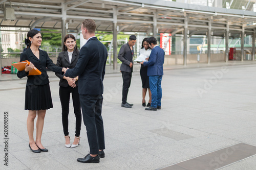 Caucasian businessman standing and shaking hand with Asian business woman and talking about business plan in the future.