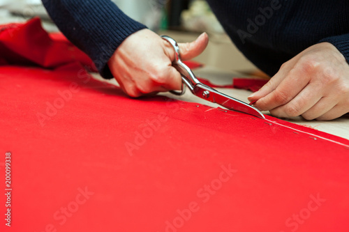 Женщина режет красную ткань ножницами.