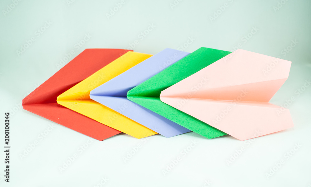 Red paper plane leading green, blue, peachy, and yellow ones on a white background, isolated. Concept (idea) of airlines, freedom, leadership, success, and individualism. Red paper plane leading green, blue, peachy, and yellow ones on a white background, isolated. Concept (idea) of airlines, freedom, leadership, success, and individualism.