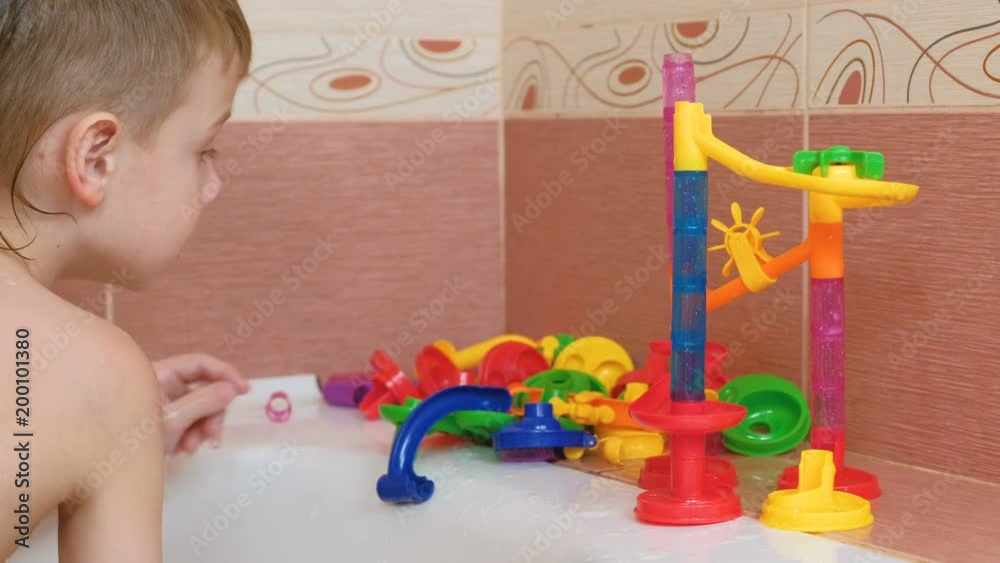 Boy builds of colored plastic piece designer slide for balls in the bathroom.