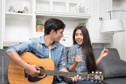 In selective focus of Young beautiful couple resting at home and playing guitar.Handsome man palying Guitar for his girlfriend learning to sing a song.