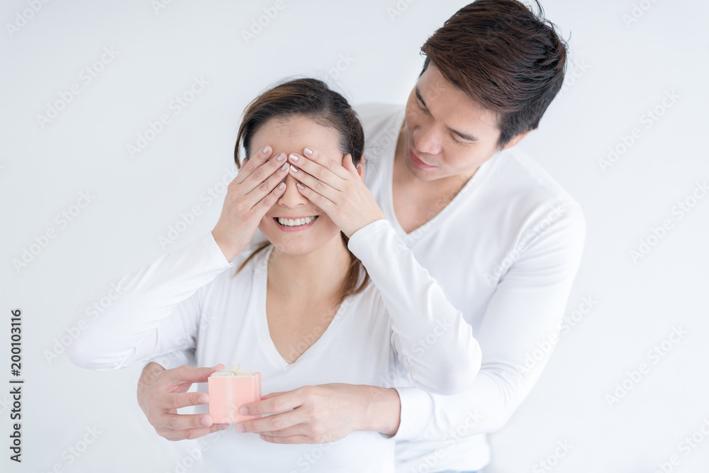 Happy husband keeps his wife eyes covered while she giving a gift. Romantic surprise. Happy husband keeps his wife eyes covered while she giving a gift. Romantic surprise.