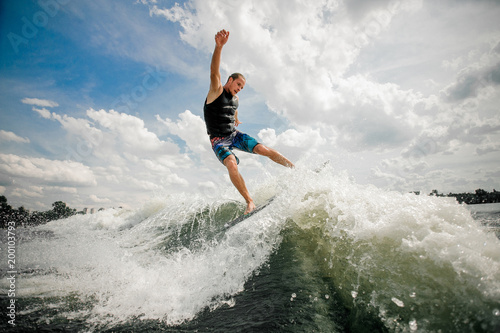 Young man wakesurfing on the board down the river against the sky