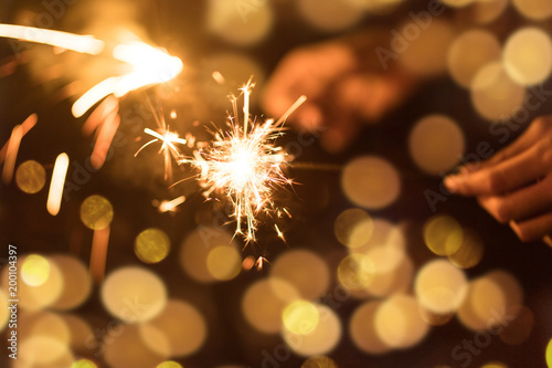 Abstract blurred of Sparklers for celebration. Friends hand holding a burn sparkler light and play together with dark background.Cinema film tone with grain.