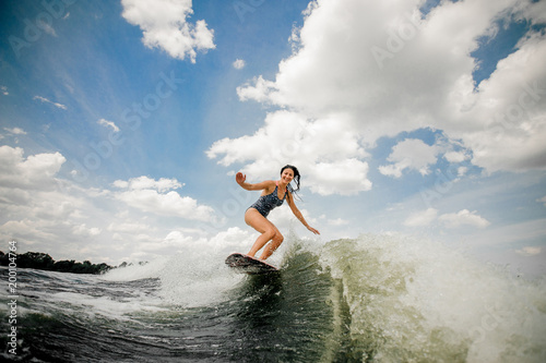 Slim smiling woman wakesurfing on the board against the sky
