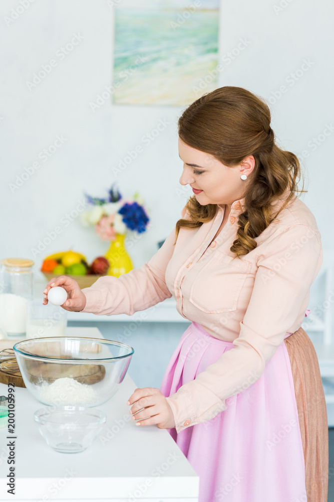 side view of beautiful woman breaking egg for dough in kitchen side view of beautiful woman breaking egg for dough in kitchen