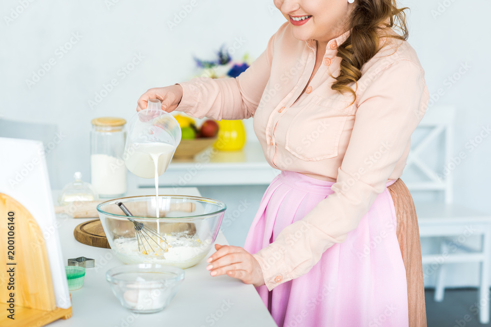 cropped image of woman pouring milk into bowl with flour at kitchen cropped image of woman pouring milk into bowl with flour at kitchen