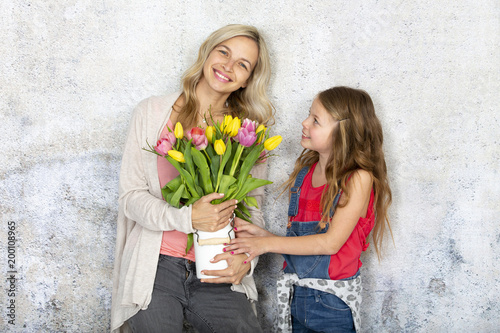 Young and blond and pretty mother gets a bouquet of colorful flowers from her daughter on Mother‘s Day