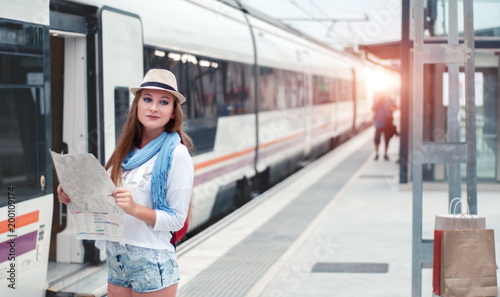Traveler girl waits train on railway platform with a map and she enjoys the upcoming trip. Travel concept.