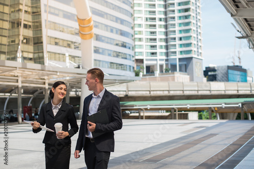 Asian business woman and Caucasian businessman wear suit walking in the city and talk about business future.
