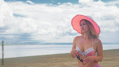 Wallpaper Mural Attractive woman in a hat stands on the beach against the blue sea. She has sunglasses and a panama on her head. On her body is a swimsuit and a silk cape. In the background are very beautiful deep Torontodigital.ca