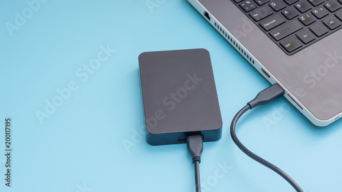 Black external hard disk connecting to a laptop on a blue background.
