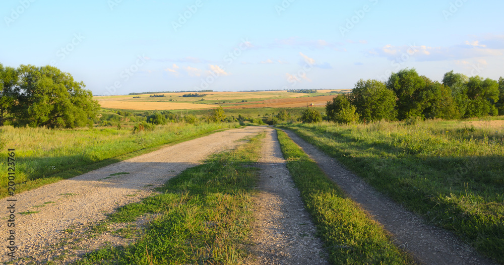 Dusty country road at sunset.Summer landscape. Dusty country road at sunset.Summer landscape.