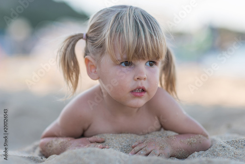 Portrait of little blondie girl lying at sandy beach
