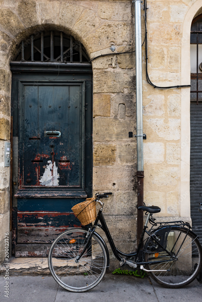 vintage bicycle with Wicker basket parked outside old grungy wooden door in the city of Bordeaux, France