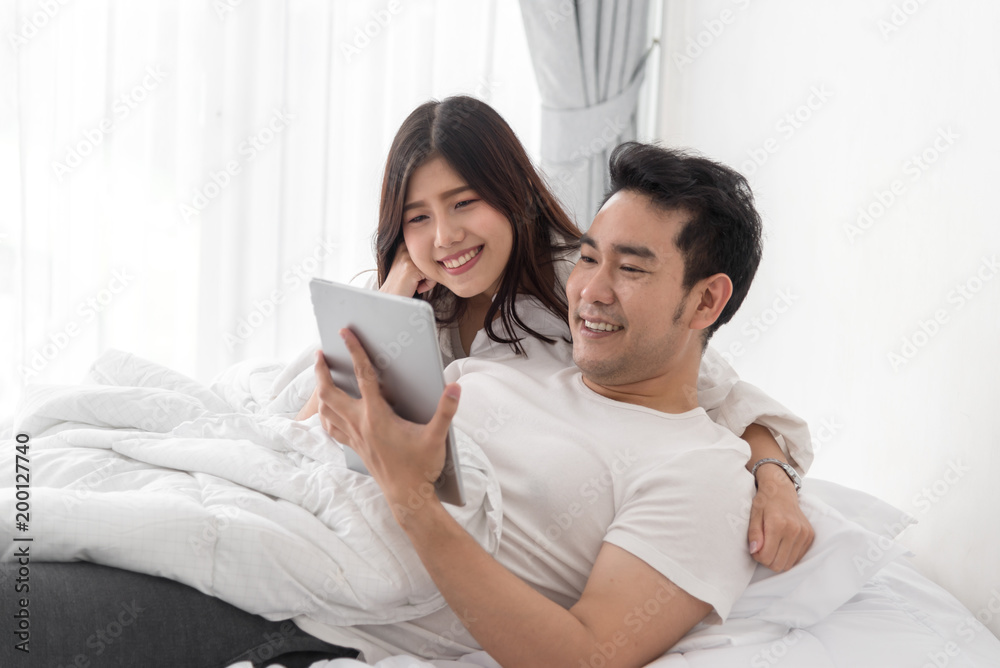 Happy Asian couple using laptop and tablet together on bed at home, lifestyle concept. Happy Asian couple using laptop and tablet together on bed at home, lifestyle concept.