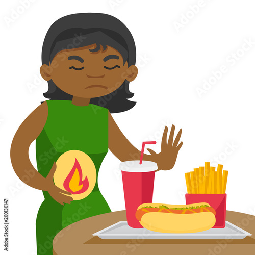 Young african woman standing near table with fast food and having stomach ache from heartburn. Girl suffering from heartburn after fast food. Vector cartoon illustration isolated on white background.