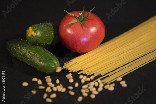 a small vegetarian grocery set of two green cucumbers, one ripe red tomato, a handful of sesame and pasta