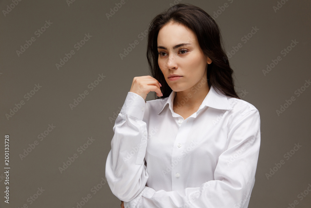 Beautiful girl in a white shirt shows emotions - thoughtfulness. On a light background. Beautiful girl in a white shirt shows emotions - thoughtfulness. On a light background.