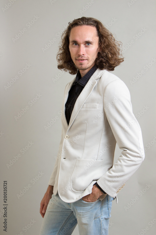 guy with long curly hair. businessman in a white jacket. on a gray background. self-confident. portraits to the waist.