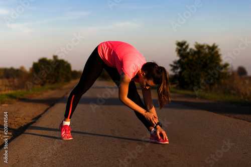Athletic woman stretching her muscles on rural road during sunset.