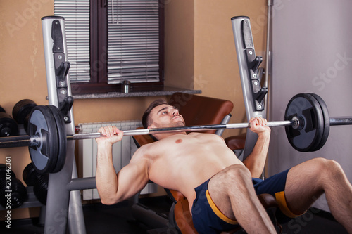 Brutal athletic man pumping up muscles on bench press