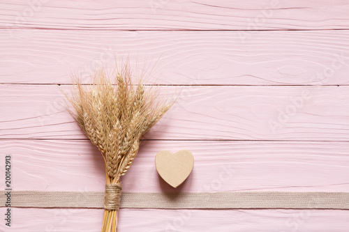 Bunch of spikelets, box in the shape of a heart lay on pink wooden background.