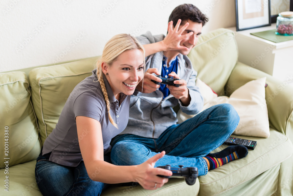 Funny young couple wearing casual clothes while playing together a video game on console at home