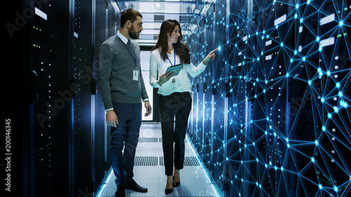 Female and Male IT Engineers Discussing Technical Details in a Working Data Center/ Server Room with Internet Connection Visualisation. photo