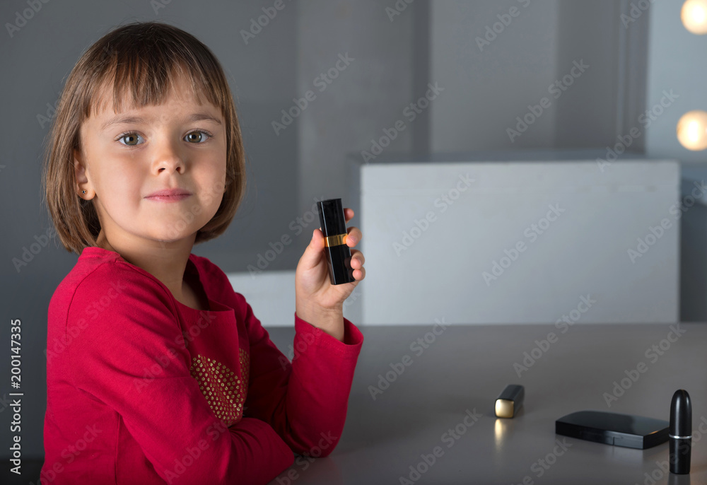 A young beautiful girl is holding a lipstick in her hand. A young beautiful girl is holding a lipstick in her hand.