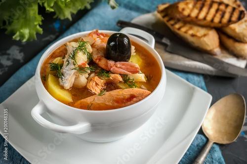 French fish soup Bouillabaisse with seafood, salmon fillet, shrimp, rich flavor, delicious dinner in a white beautiful plate.