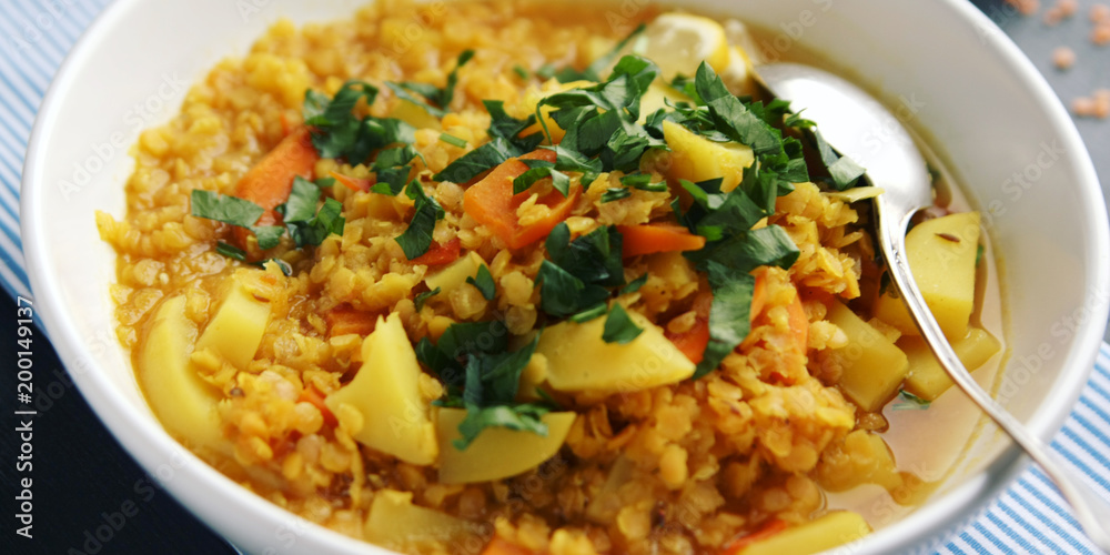 Red lentil stew with potato, carrot and turmeric. Toned photo. Healthy lunch on the round white plate. Colorful vegan dish with potato, carrot and turmeric. European cuisine. Vegetarian. Red lentil stew with potato, carrot and turmeric. Toned photo. Healthy lunch on the round white plate. Colorful vegan dish with potato, carrot and turmeric. European cuisine. Vegetarian.