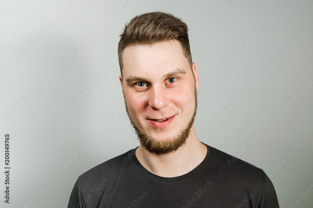 Fototapeta premium Young smiling guy with beard and modern hairstyle on gray background.