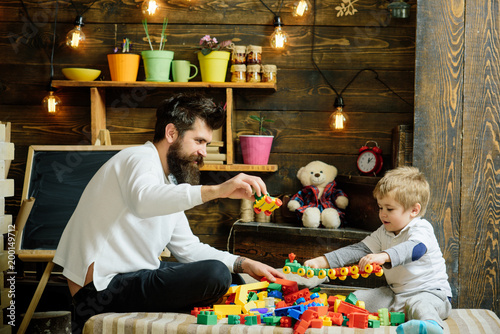 Dad and child play with toy cars, bricks. Father and happy son play with constructor. Fatherhood concept. Nursery with toys and chalkboard on background. Family playing with constructor at home.