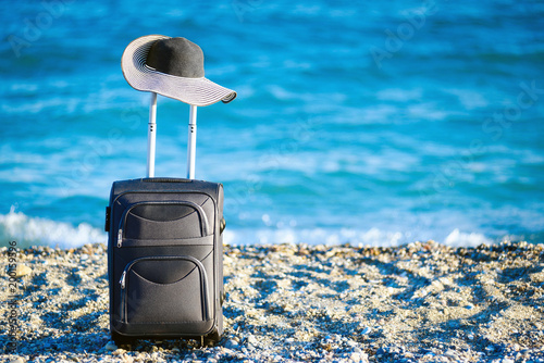 suitcase and hat on beach and sea on background photo