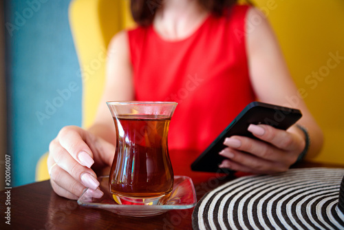 women in red dress and hand with phone and turkish tea and hat on the wooden table.