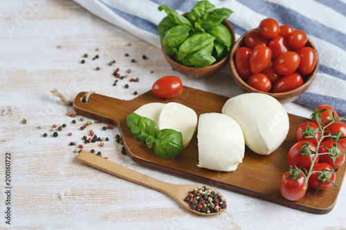 Mozzarella cheese with red tomatoes and basil leaves, pepper, olive oil, wooden desk, healthy food concept
