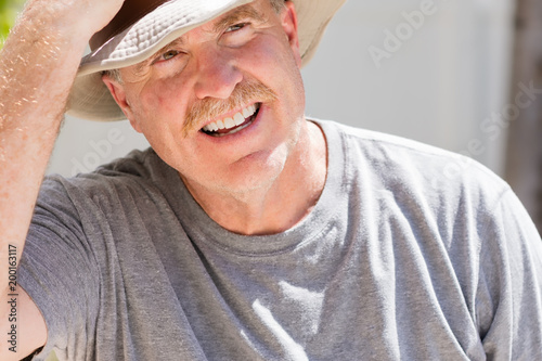 Senior male puts on his cowboy hat on hot sunny day