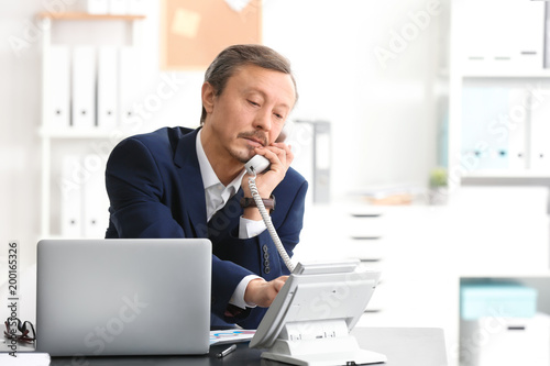Mature man talking on phone while working indoors