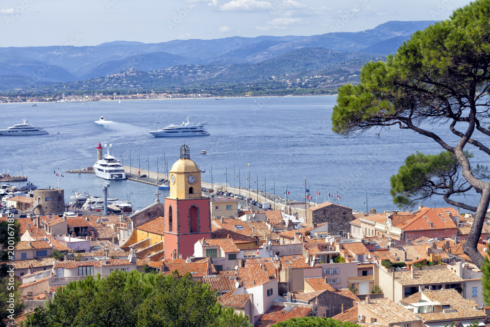 Panoramic view of Saint Tropez, Mediterranean chic fishing village in French Riviera, over roofs of old historical houses, port pier with super yachts .